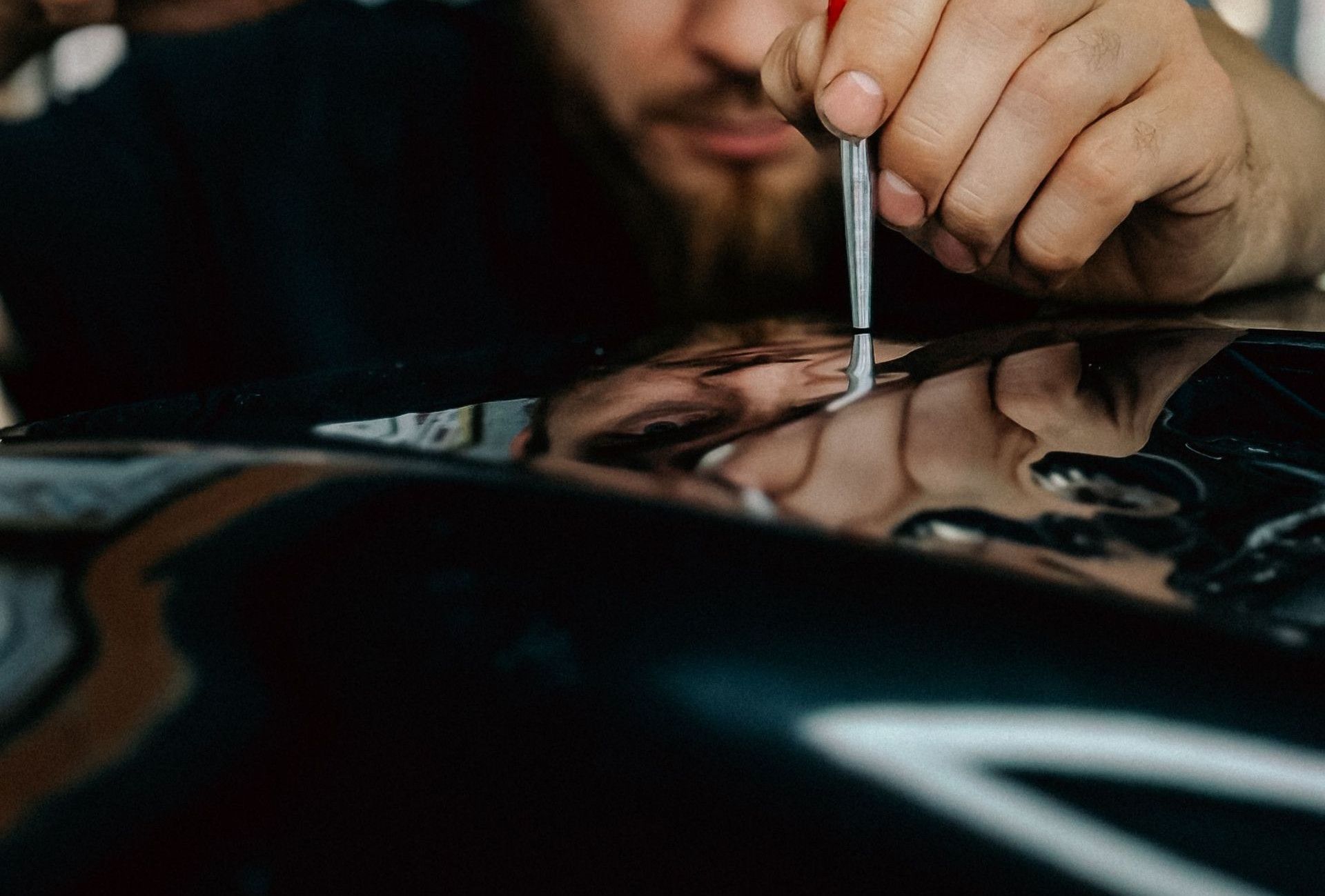 Mechanic expertly repairing car dent using specialized tool in workshop.