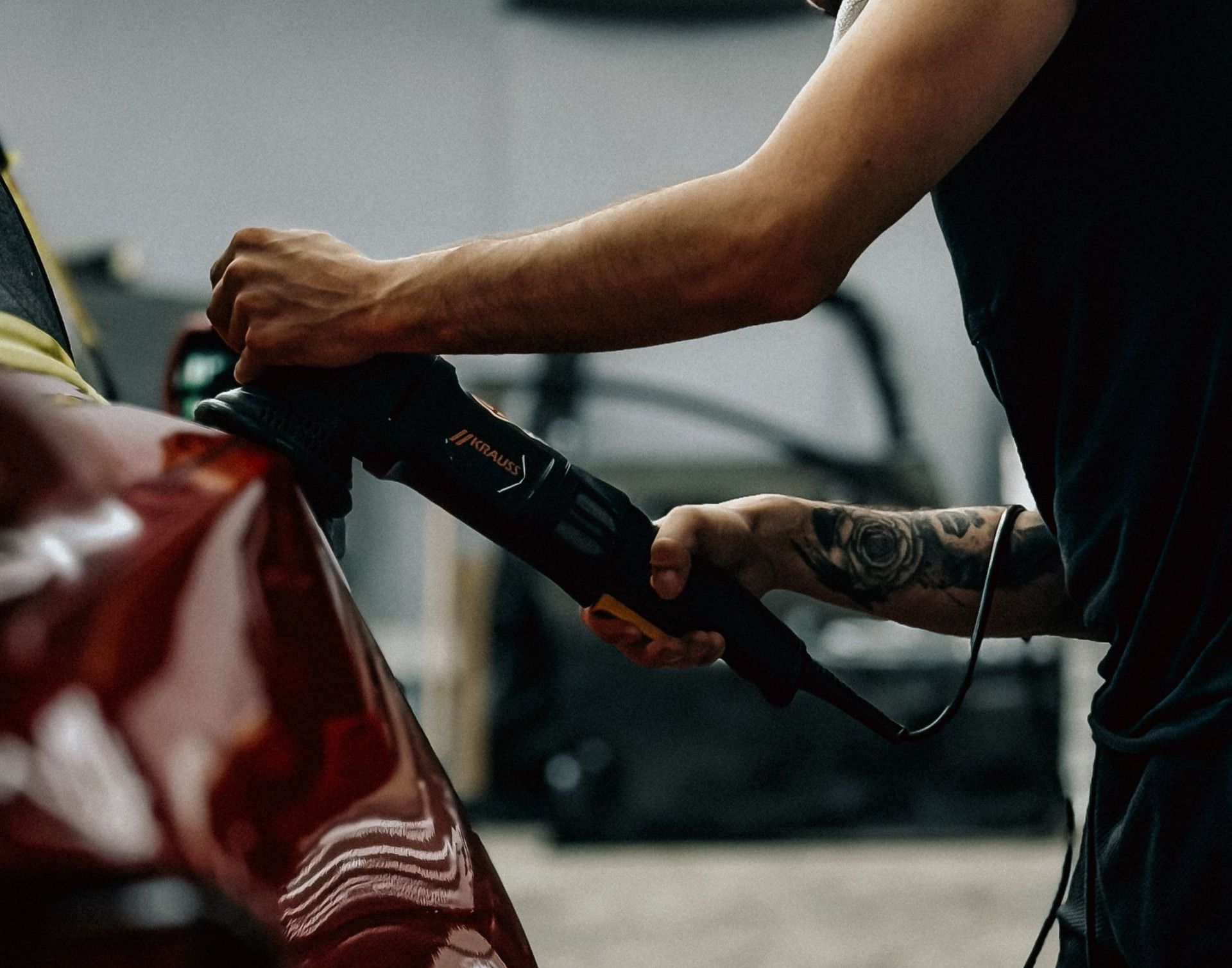 A focused man diligently polishes a red car in a modern garage.